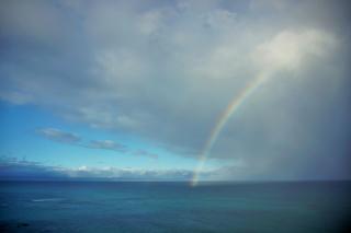A rainbow connecting the blue sea to big, white clouds in a blue sky.