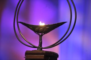 A lit Unitarian Universalist chalice before a purple background.