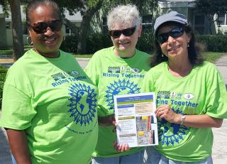 three women in green Rising Together tee shirts holding an outreach sheet