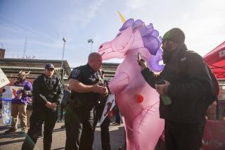 Police officers tell the Rev. Forrest Gilmore, who is dressed as a pink and purple unicorn, to leave before arresting him at a farmers' market in Bloomington, Indiana, where he and others have been protesting a vendor with ties to white supremacy groups