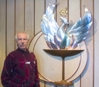 Photo of congregant Antonio Borra of the UU Congregation of Atlanta standing next to a statue of a phoenix arising from a flaming chalice.