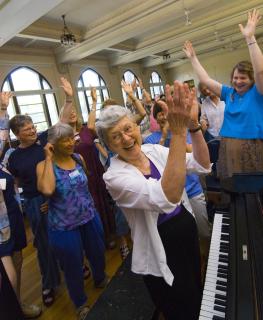 Carolyn McDade leads exuberant singers from piano