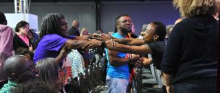 Ndidi Achebe, left, and Ebonie Remsey link arms during the closing worship as the gathering sang “I need you to survive.”