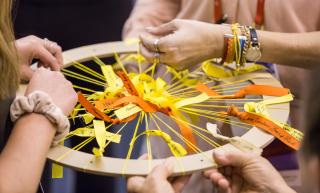 Participants weave ribbons with written messages into a circle frame during the cuups (Covenant of UU Pagans) Summer Solstice celebration at GA 2019.
