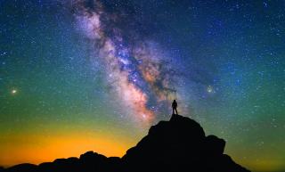 Stock photo of a figure silhouetted against a galaxy night sky.