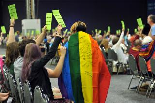 Youth sign a rainbow flag as delegates raise voting cards at 2016 GA