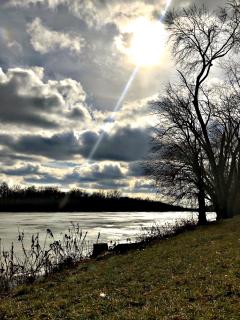 Photograph entitled "Farnsworth Metropark, Waterville, Ohio (February 2018)" of a water, clouds, trees, and sun scene.
