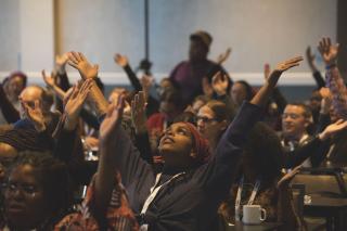 People raise their arms during a time of spiritual grounding at the BLUU Harper-Jones Theological Symposium on November 1