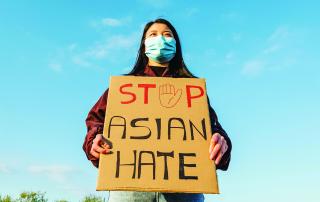 Stock photo of Asian person holding a sign saying "STOP ASIAN HATE" wearing a mask