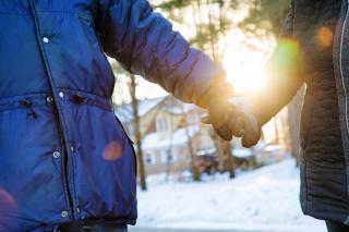 Stock photo of 2 people in winter coats holding hands in winter at sunset.