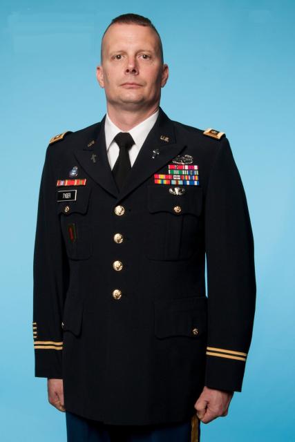 George Tyger stands against a blue background in his dress uniform, which includes many military insignia.